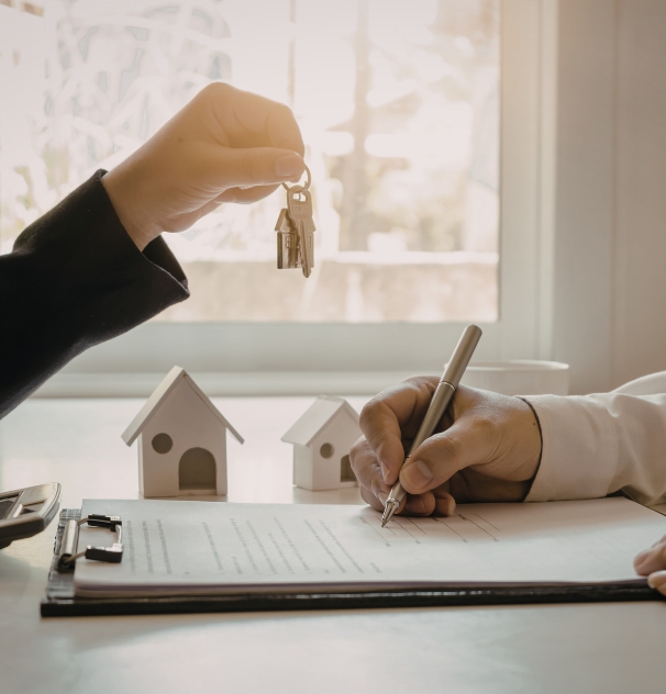 Manos entregando unas llaves mientras otra persona firma un contrato, representación visual del proceso de compra asesorada de vivienda o inversión.