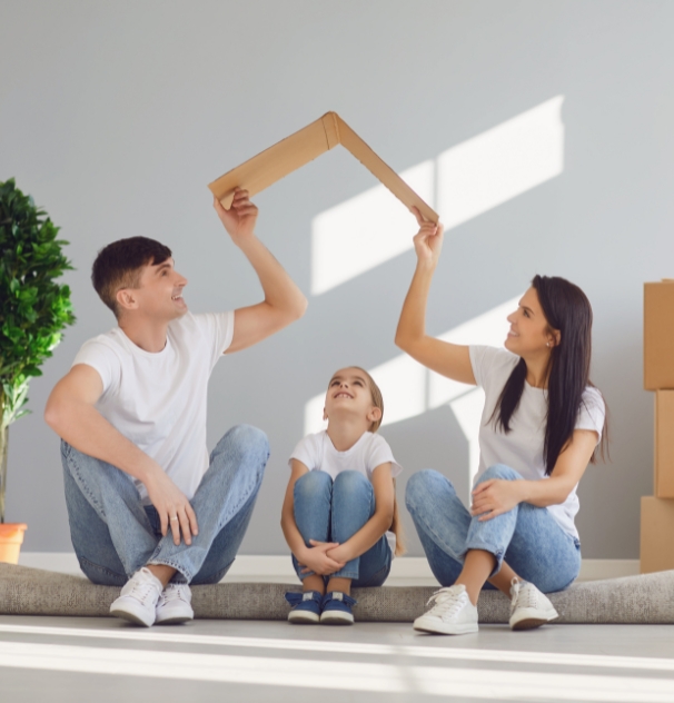Familia sonriente cubriendo a su hija con un cartón a modo de tejado, representando la protección y los seguros familiares.